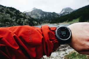 Jam tangan outdoor tangguh di pergelangan tangan, dengan latar belakang gunung atau hutan.