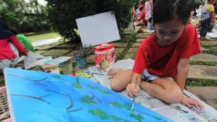 Gambar seorang siswa sedang melukis di kanvas besar di sebuah studio seni yang terang.
