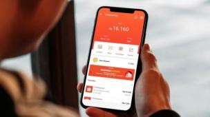 Layar smartphone menampilkan aplikasi e-commerce dengan produk handphone dan latar belakang kota Bogor.
