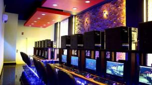 Bagian dalam warnet yang terang di malam hari, menunjukkan beberapa orang masih fokus di depan komputer.