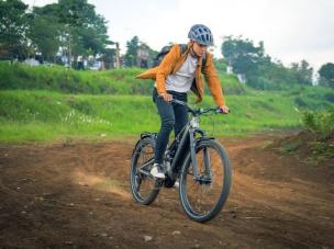 Gambar sepeda gunung elektrik Specialized Levo SL sedang dikendarai secara agresif menuruni jalur gunung yang teknis dengan vegetasi hijau subur, menonjolkan kemampuan dan bantuan elektriknya, dengan 