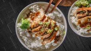 Hidangan nasi bowl dengan penataan makanan yang estetik di atas meja kafe dengan interior modern.