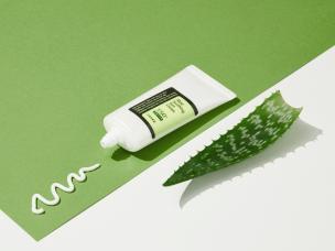 Gambar tube COSRX Aloe Soothing Sun Cream di latar belakang yang ramping dan minimalis, menyiratkan produk yang bersih dan sederhana untuk pria, dengan latar belakang samar Medan.