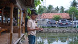 Orang sedang memancing di kolam pemancingan dengan saung-saung di sekelilingnya, suasana tenang.