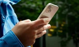 Tangan sedang memegang smartphone kompak dengan satu tangan, menunjukkan kemudahan penggunaan.