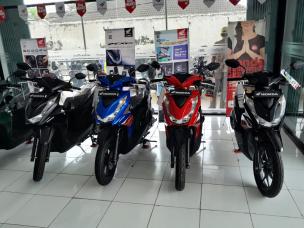 Gambar showroom motor yang luas menampilkan berbagai model dan warna motor matic.
