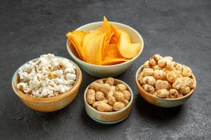 Gambar beberapa kemasan snack ekstrudat jagung dengan berbagai rasa, diletakkan di samping mangkuk berisi isinya.