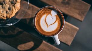 Gelas kopi dengan latte art di atas meja kayu yang estetik.