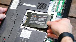 Tangan memegang SSD dekat slot upgrade laptop