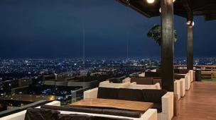 Teras restoran di ketinggian dengan pemandangan lampu kota dari jauh.