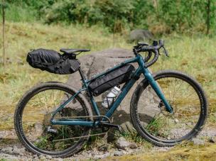 Gambar sepeda touring Surly Ogre yang terisi penuh di jalan tanah terpencil yang indah dengan lanskap alam yang luas di latar belakang, menonjolkan ketangguhan dan kesiapan ekspedisinya, dengan latar 