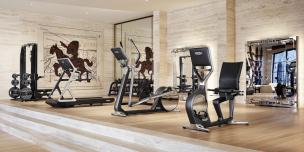 Interior gym modern dengan berbagai alat fitness dan beberapa orang sedang berolahraga.