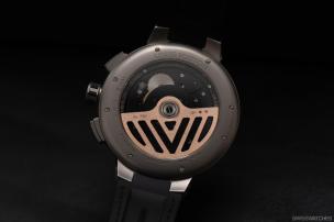 Jam tangan otomatis dengan case belakang transparan menunjukkan mesin bergerak, di latar belakang buku tentang horologi.