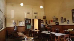 Gambar interior Kopi Aroma dengan karung kopi dan sudut baca.