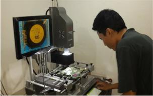Teknisi sedang memperbaiki laptop di meja kerja yang dipenuhi peralatan elektronik.