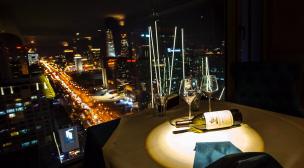 Interior restoran mewah dengan pemandangan kota malam dari jendela tinggi.