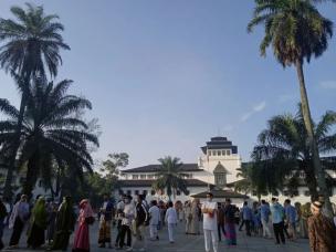 Orang-orang sedang jogging di Lapangan Gasibu Bandung dengan Gedung Sate di latar belakang.