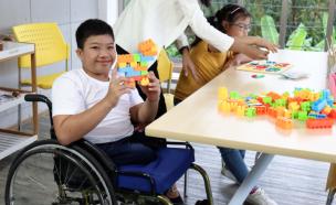 Gambar seorang guru berinteraksi dengan siswa menggunakan kursi roda di kelas, menunjukkan dukungan dan inklusivitas.