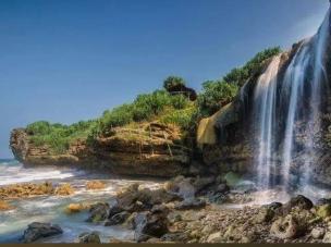 Gambar Pantai Jogan dengan air terjun langsung ke laut dan tebing berbatu.