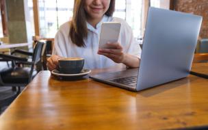 Seseorang sedang bekerja dengan laptop di meja kafe yang rapi dengan secangkir kopi dan beberapa stop kontak.